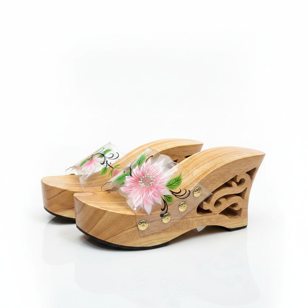 A pair of wooden wedge mule sandals with carved details and a clear strap decorated with a pink and green flower, set against a plain white background.