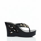 A single black wedge sandal with a cutout platform sole and a decorative embellished toe strap, shown from a side profile on a white background.