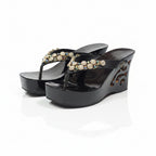 A pair of black platform wedge sandals with cutout details and ornate gold-tone embellishments on the straps, set against a plain white background.