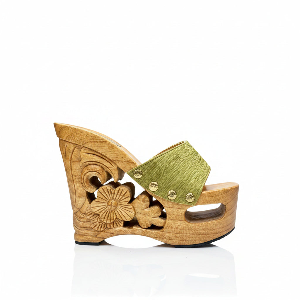 A single wooden wedge sandal with a carved floral design on the heel, a light brown wood platform, and a textured olive green strap adorned with three gold-tone rivets, shown against a plain white background.
