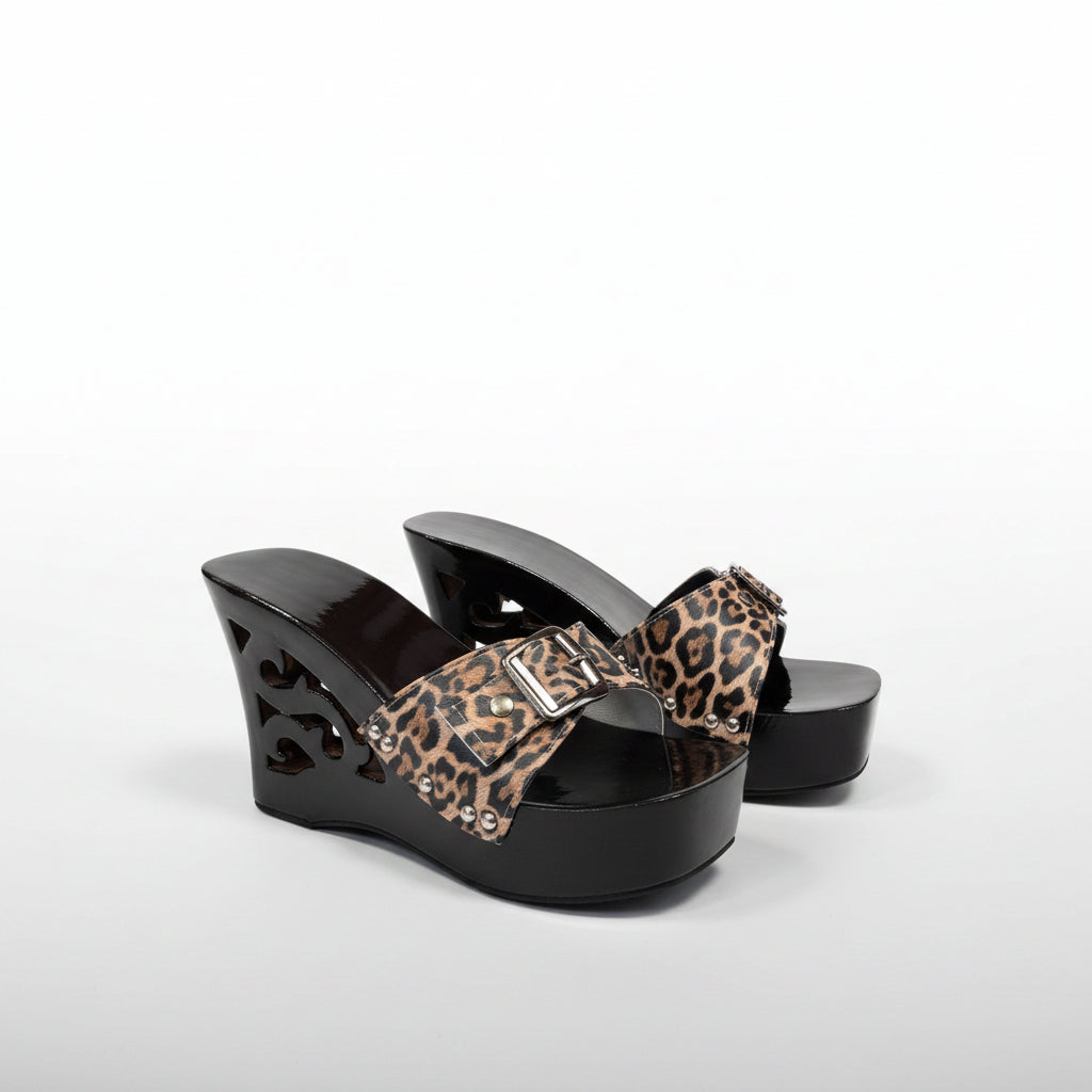A pair of women's wedge mule sandals with glossy black cutout platforms and straps featuring a leopard print pattern in brown, beige, and black.