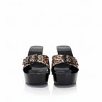 A pair of women's platform mule sandals featuring glossy black patent leather soles and straps, accented with leopard print fabric bows on the front.
